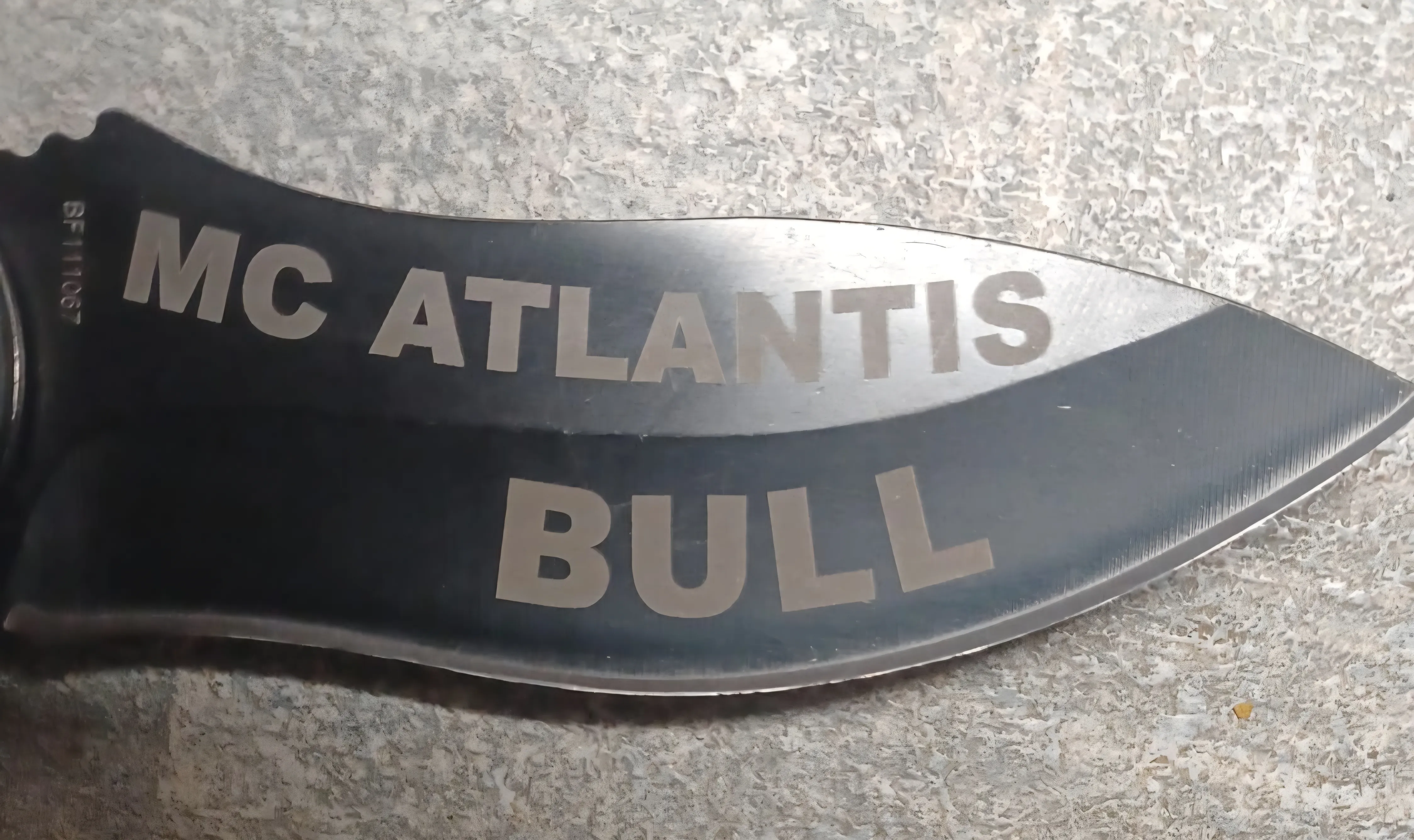 Detailaufnahme einer Messergravur mit MC Atlantis und Bull auf schwarzer Klinge